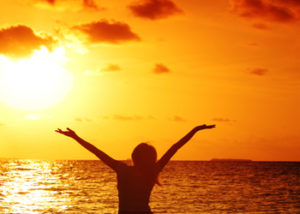 woman holding up her arms in sunset - how to describe happiness in writing