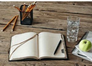 journal with a glass of water and an apple close by