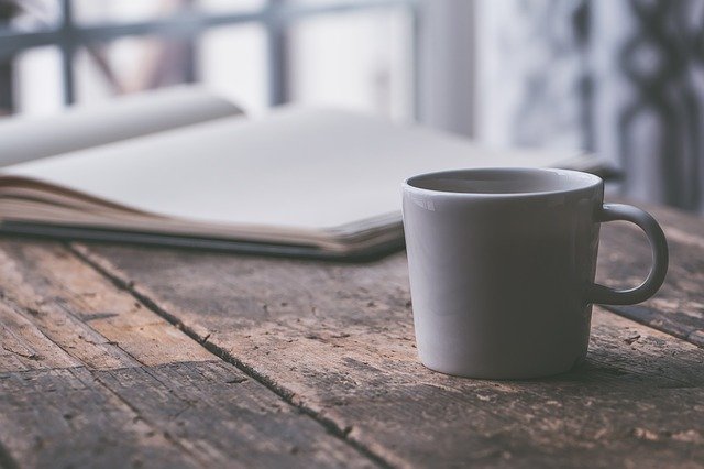 Coffee cup and open journal, window in background