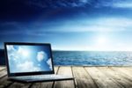 laptop on pier overlooking ocean, reflecting sky and clouds