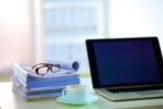 a computer, eyeglasses, and a stack of manuscripts ready for developmental editing