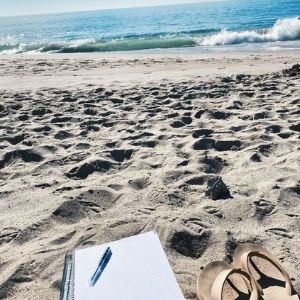 sandals and a notebook in the sand, with the ocean waves in the distance