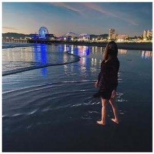 Bryn Donovan standing in the ocean at night, wearing a mask, with the lights of Santa Monica Pier in the background