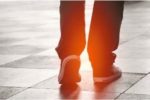 feet walking on a sidewalk with light shining behind
