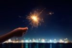 a hand holding a sparkler against the night sky - representing being positive in a negative situation