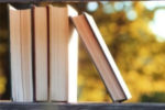 a stack of books with fall leaves in the backgrouns