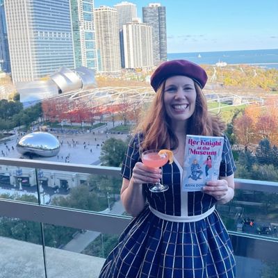 author Bryn Donovan on Cindy’s Rooftop in Chicago, holding her book HER KNIGHT AT THE MUSEUM and a cocktail, the city of Chicago in the background