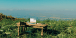 desk with laptop and chair sitting on a grassy bluff overlooking a valley