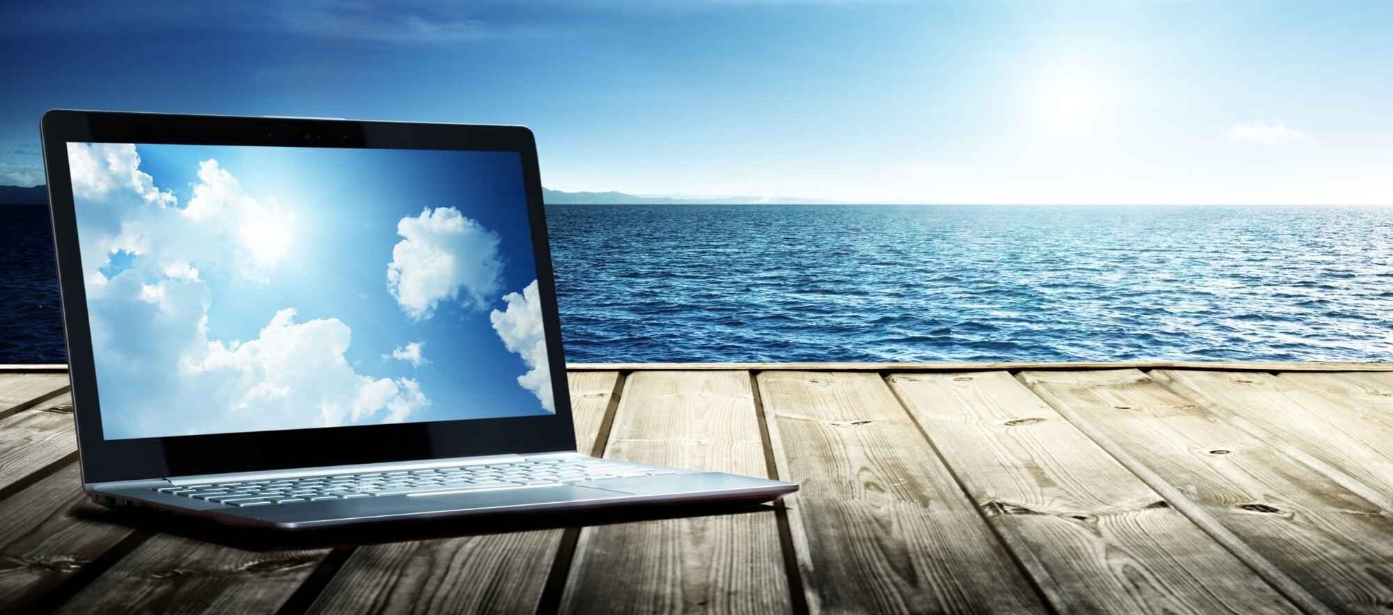 laptop, ocean, blue sky and clouds reflected on computer screen, suggesting writing inspiration