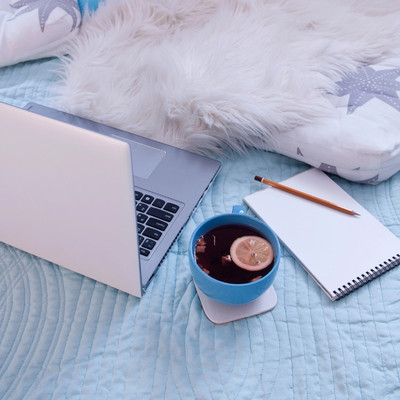 cozy writer image laptop, tea, notepad, pencil, and fluffy blanket, all on a bed