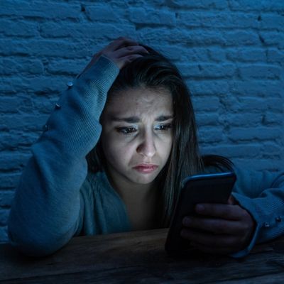 woman holding phone and looking traumatized, illustrating the effects of negative social media algorithms