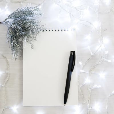 blank pad of paper and pen surrounded by twinkly string of lights and evergreen branch