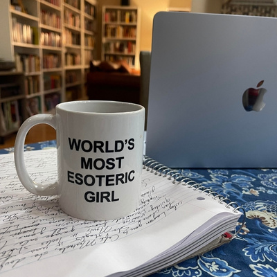 photo of Bryn’s kitchen table with a notebook full of handwriting, her laptop, and a mug that reads “World’s Most Esoteric Girl