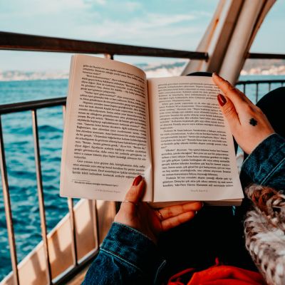 the hands of a woman holding a summer thriller book while reclining on the deck of a boat